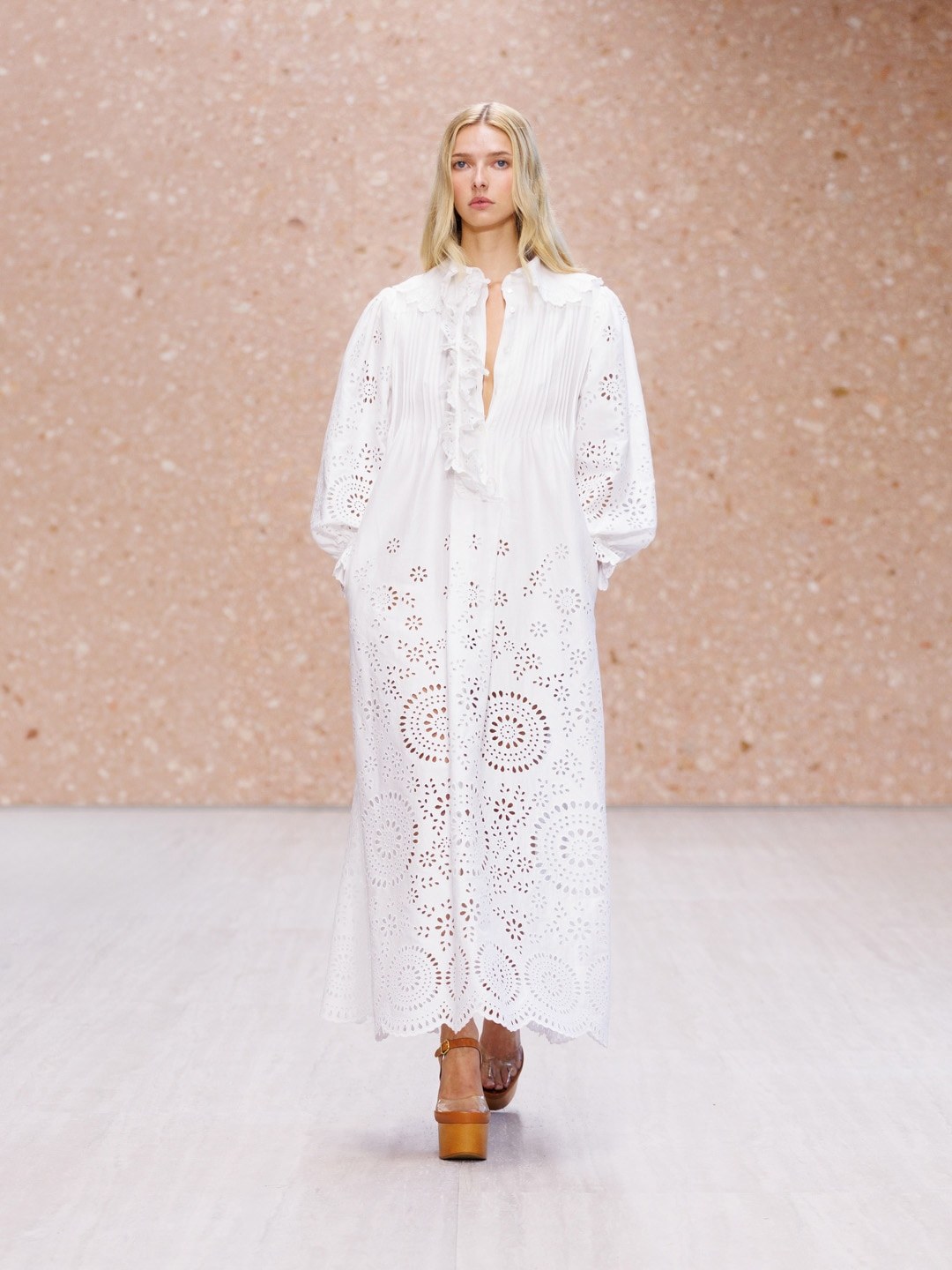 A model walks Chloé's Summer 2027 runway in a white broderie anglaise maxi dress with a ruffled placket, balloon sleeves and brown platform sandals