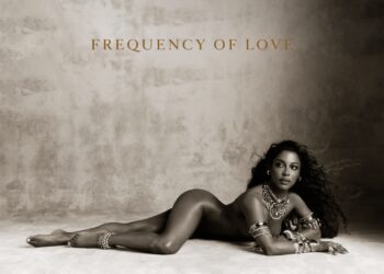 Official cover art for Victoria Monét's album Frequency of Love, a sepia-toned portrait of Monét reclining on the floor in layered gold jewelry beneath the album title